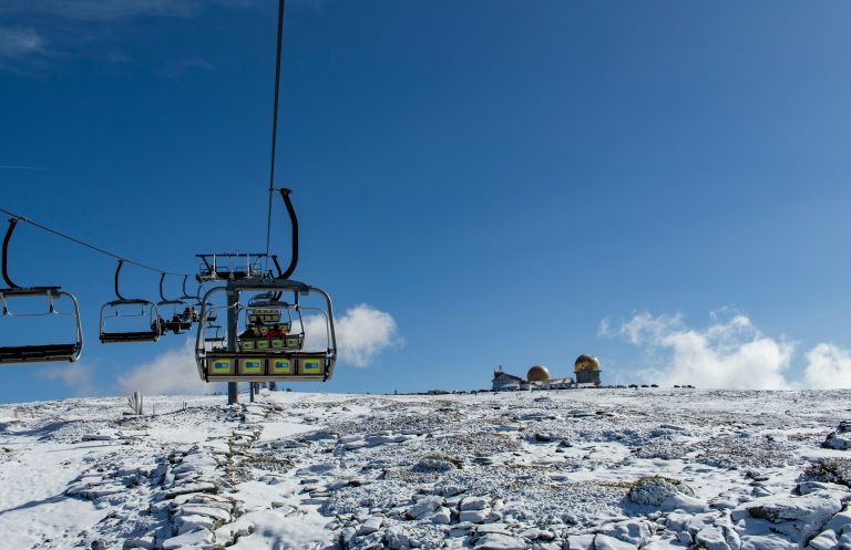Ski lift leading to a snow-covered plateau with observatory under a clear blue sky in Serra da Estrela.